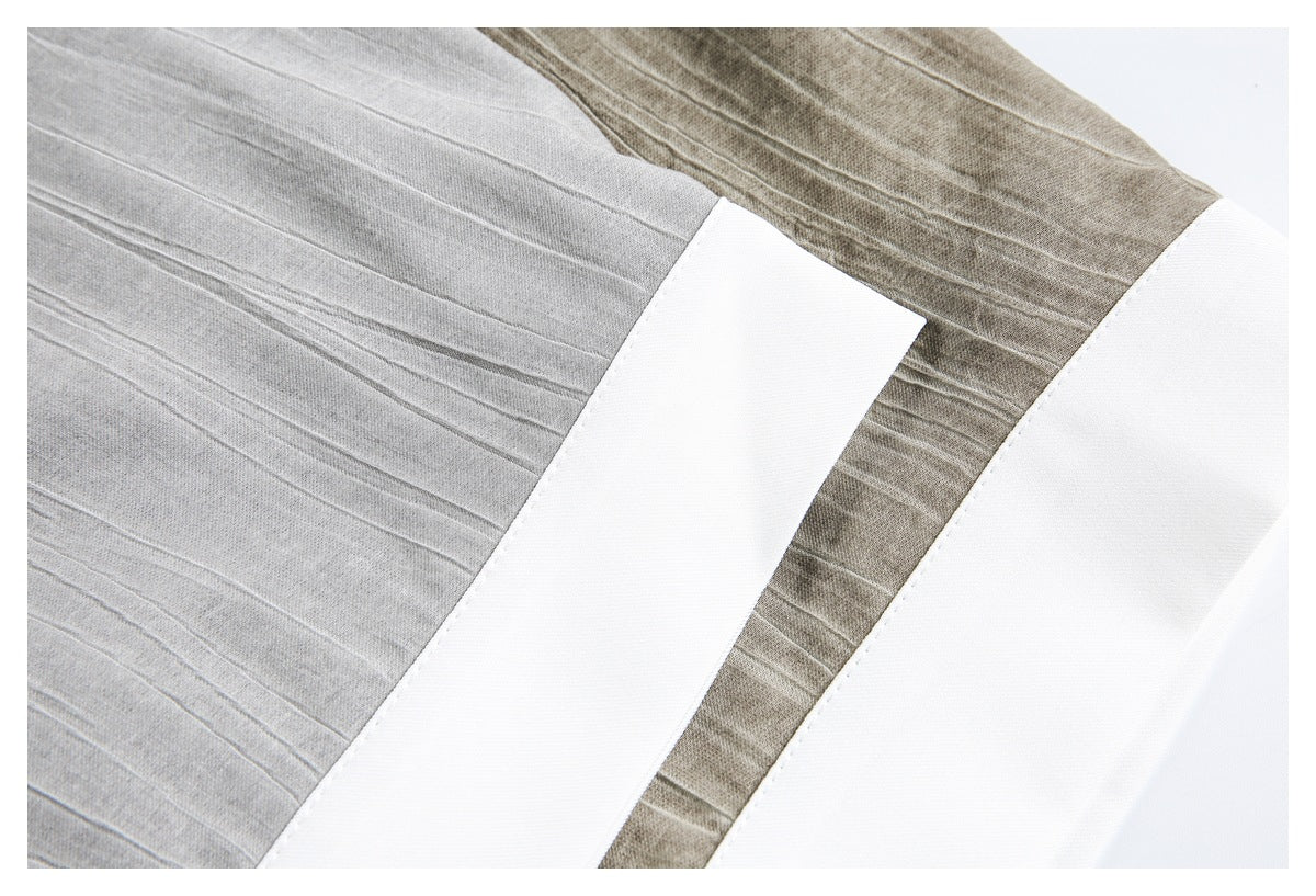 Close-up of a gray textured garment with raised lines beside a white panel and taupe section.