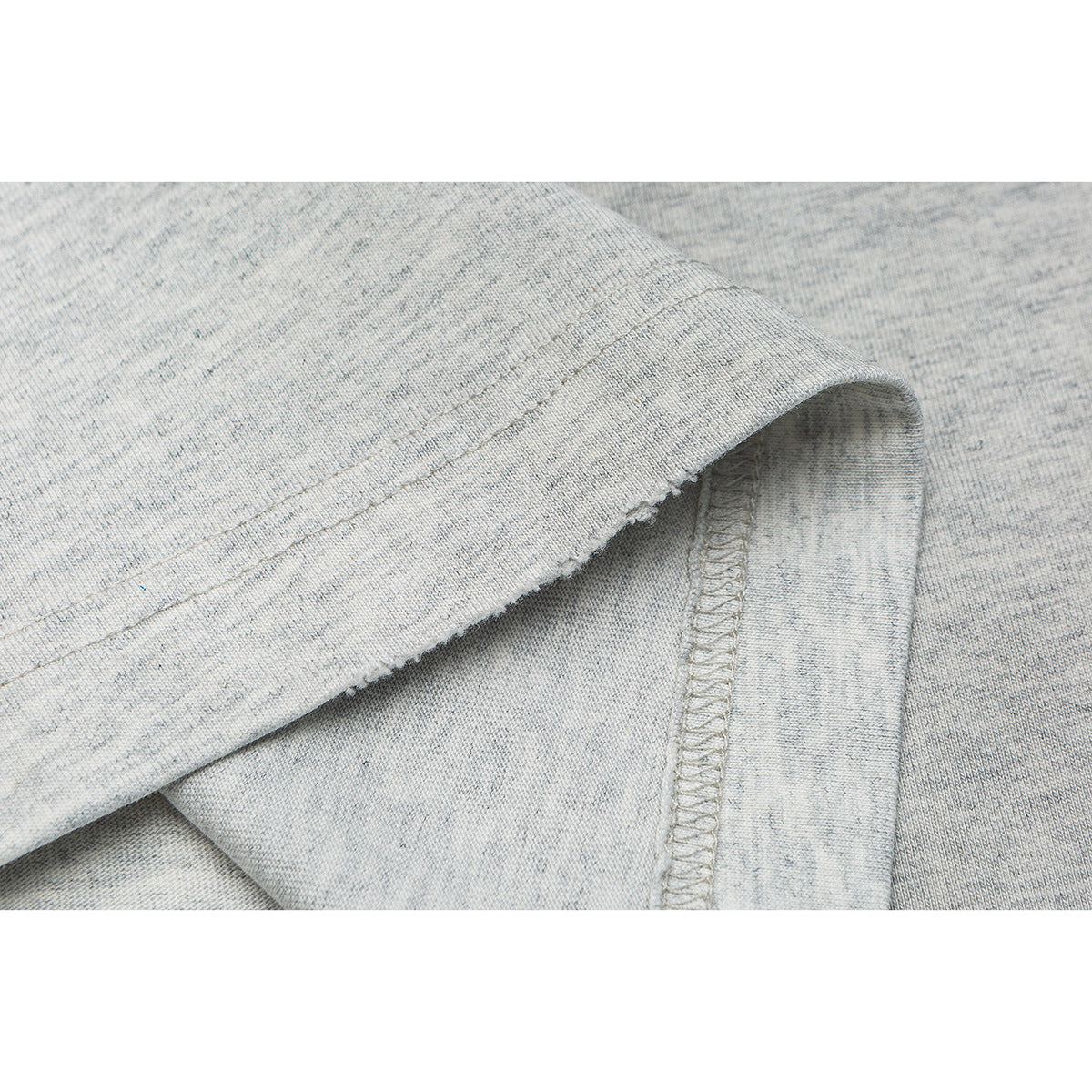 Close-up of the folded hem and overlocked seam on a light gray T-shirt.