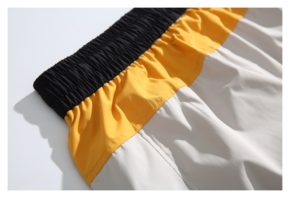 Close-up of black elastic waistband and mustard-yellow and off-white color-blocked shorts panels.
