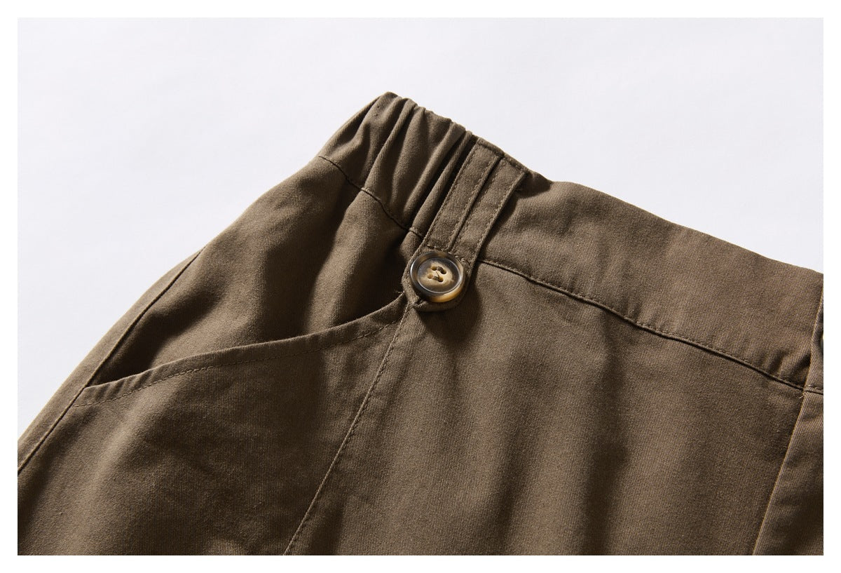 Close-up of brown trousers showing the gathered waistband, belt loop, button, and angled pocket opening.