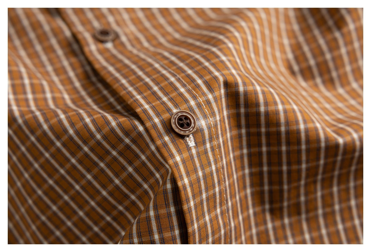 Close-up of a brown button and buttonhole on the brown, cream, and dark plaid shirt.