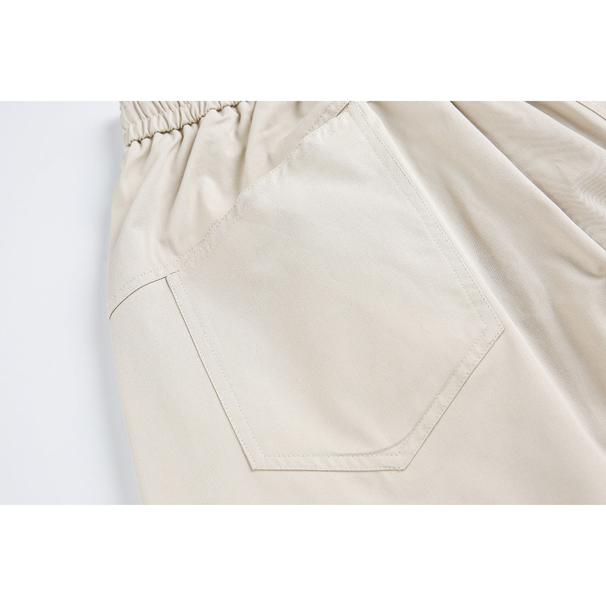 Close-up of beige pants showing a large angular stitched pocket and gathered elastic waistband.