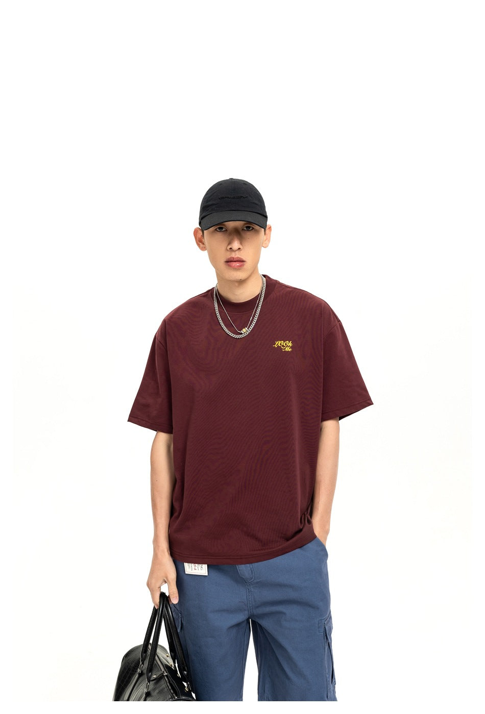 Upper-body view of a model wearing a burgundy oversized T-shirt with small yellow chest script.
