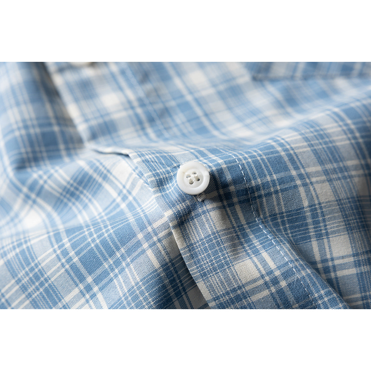 Close-up of a white button and stitching on blue-and-white plaid shirt fabric.