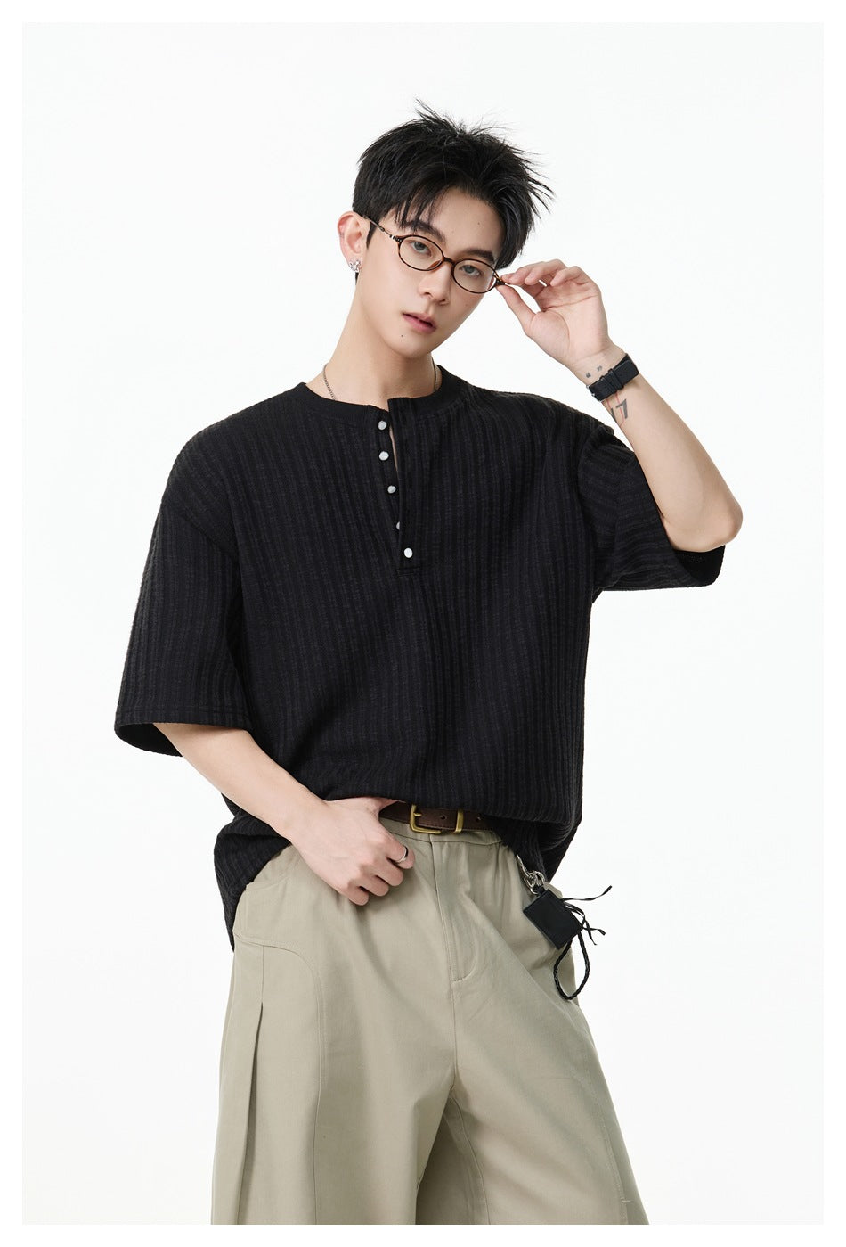 Model wearing a black ribbed Henley T-shirt with the snap placket partly open, with khaki trousers and a brown belt