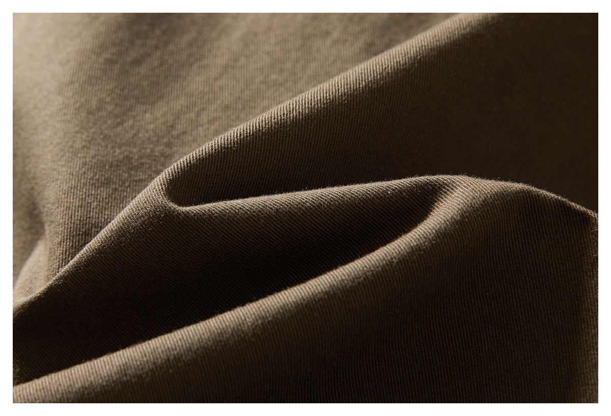 Extreme close-up of brown trouser fabric showing its fine diagonal weave and draped folds.