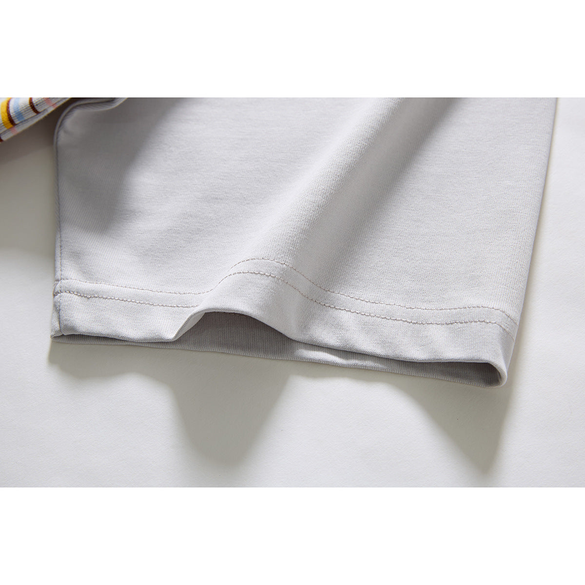 Close-up of the plain light gray sleeve and stitched hem, with a small section of striped shirt visible.