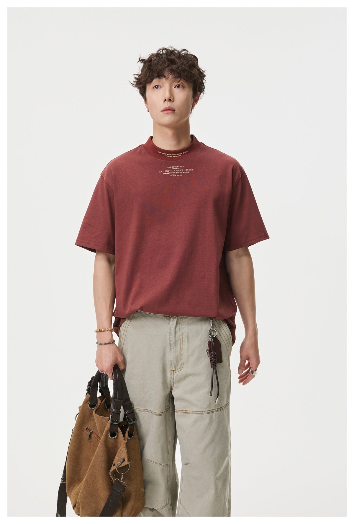 Model wearing a burgundy short-sleeve T-shirt with small cream text at the chest and high neckline.