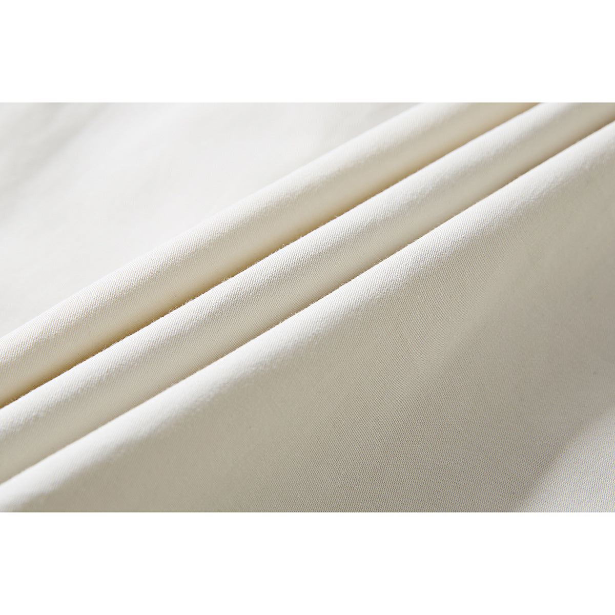 Close-up of ivory shirt fabric arranged in diagonal folds, showing its surface and drape.
