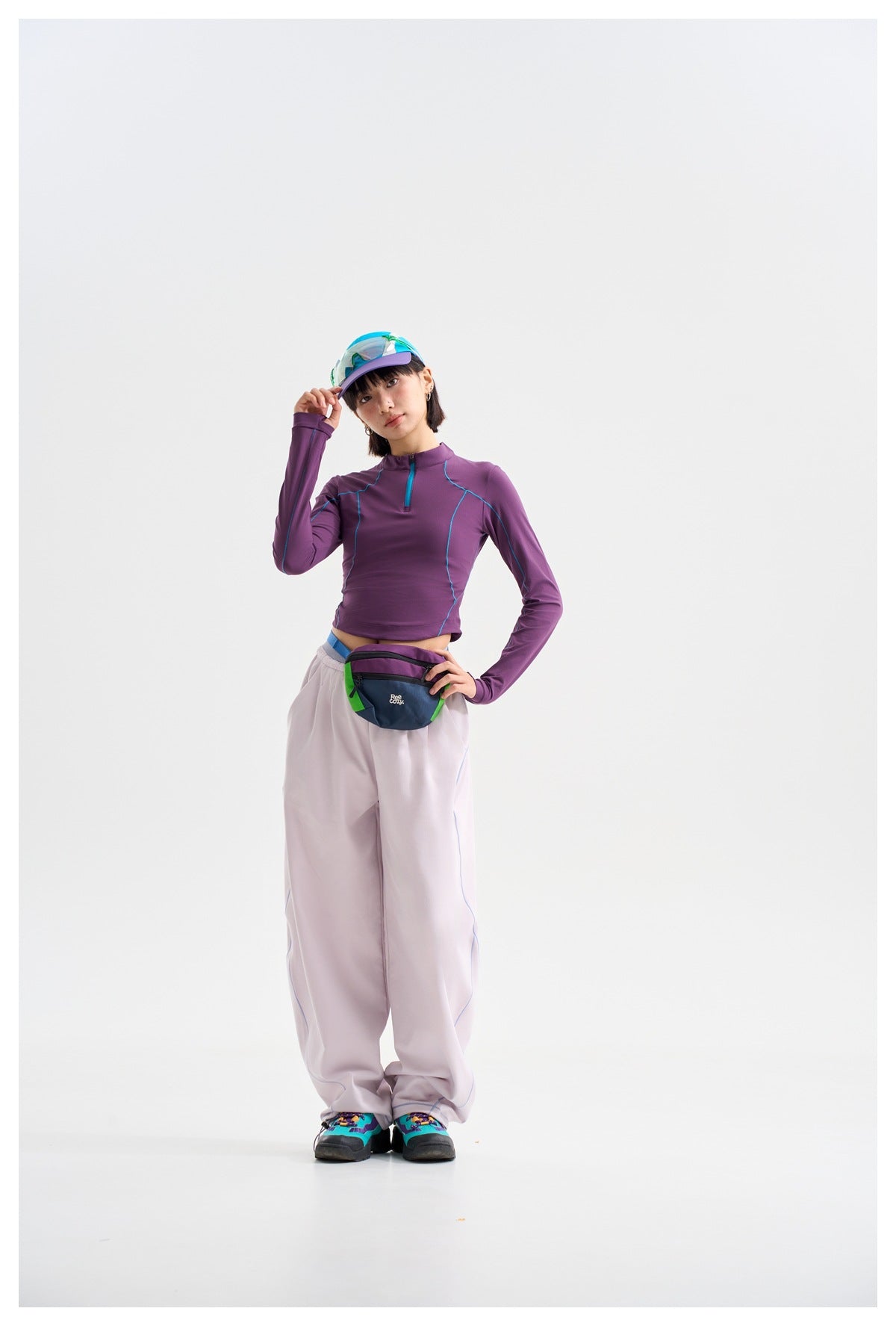 Model wearing a purple long-sleeve quarter-zip top with turquoise seams and loose pale lavender pants.