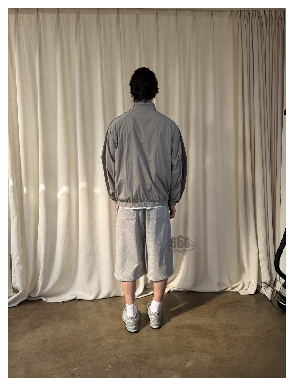 Back view of a model wearing light gray knee-length shorts beneath a gray jacket.