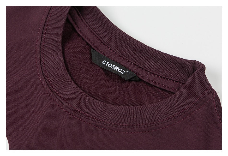 Close-up of a dark burgundy T-shirt's ribbed crew neck, stitching, and inside brand label.