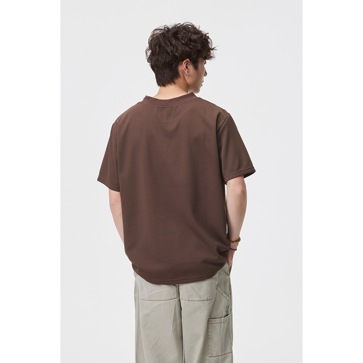 Back view of a model wearing a plain brown short-sleeve T-shirt with beige trousers.