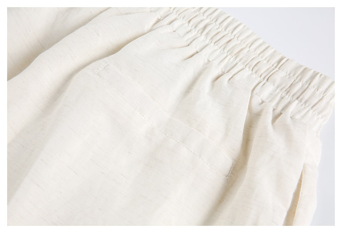 Close-up of cream trousers showing an elastic waistband and a front pocket.