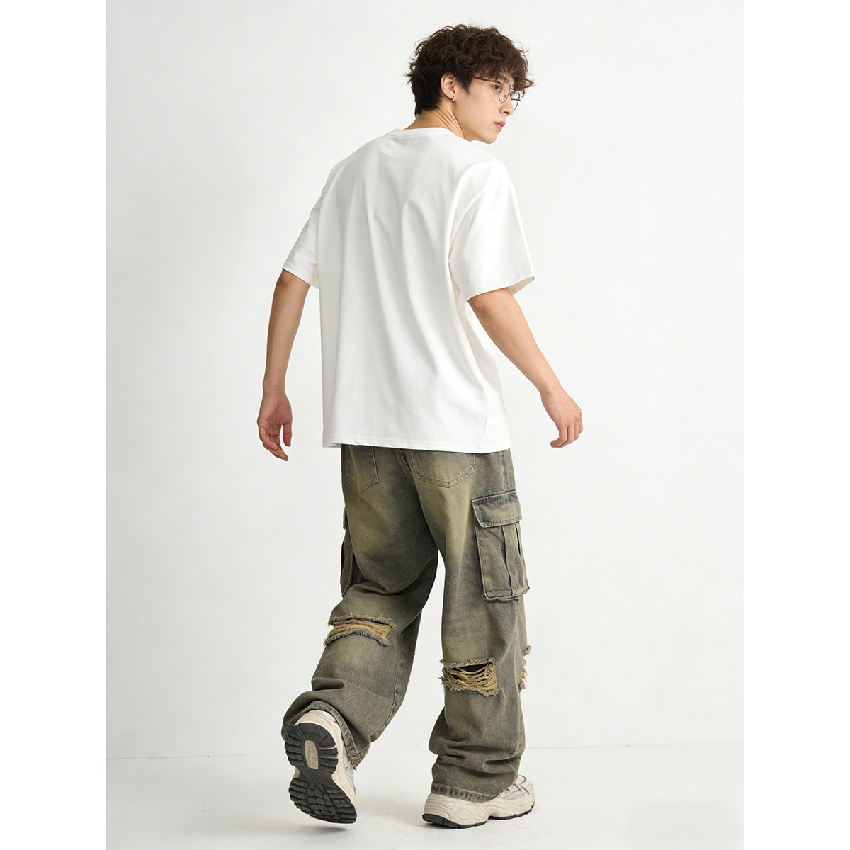 Rear view of a model in a white oversized T-shirt and distressed olive-gray cargo pants.