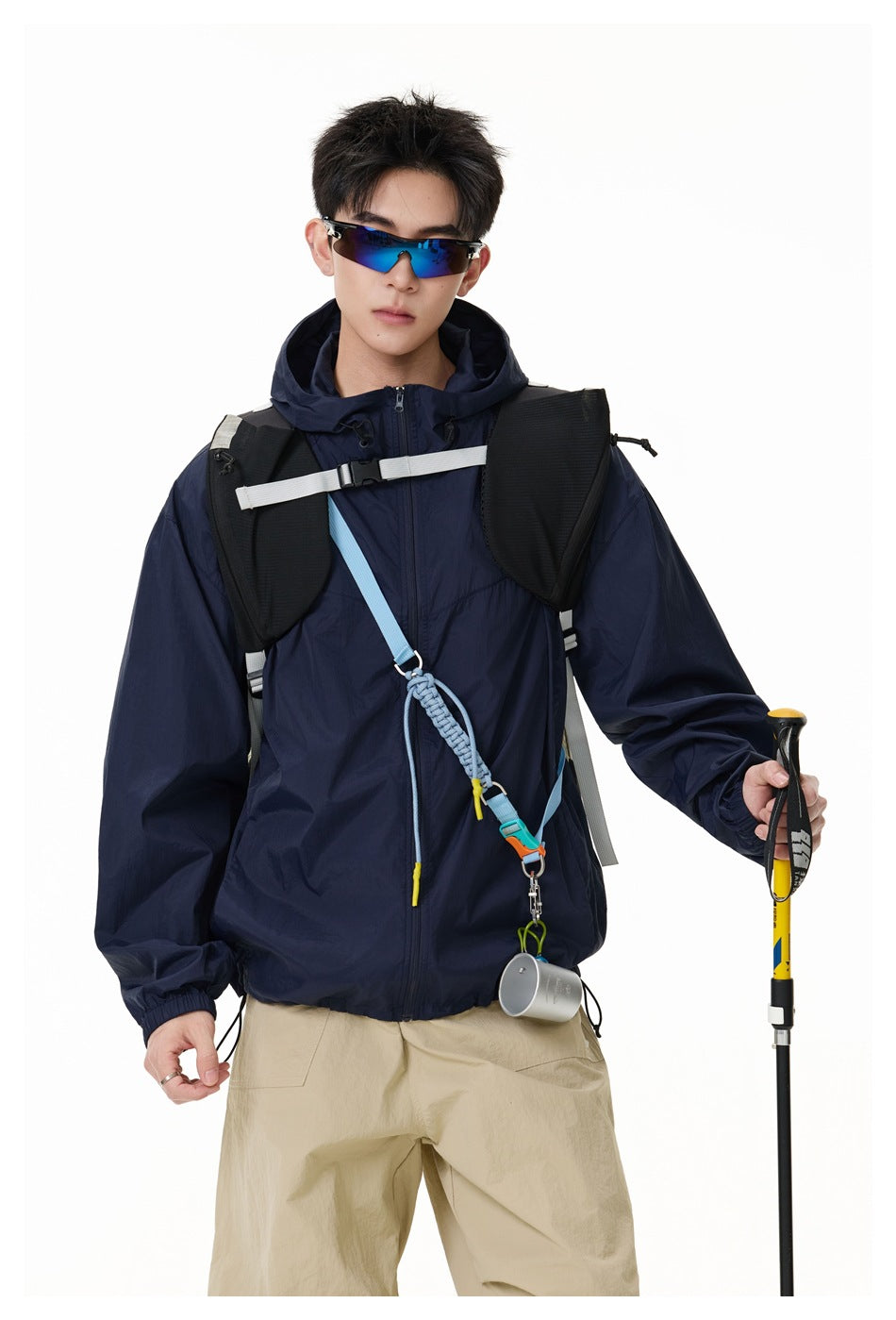 Model wearing navy hooded zip jacket with backpack, sunglasses and trekking pole, close three-quarter view