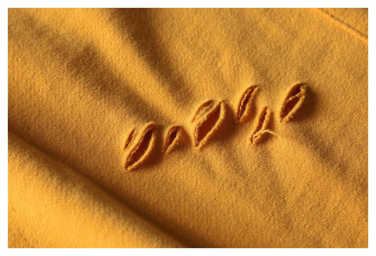 Close-up of mustard fabric showing raised, distressed stitched lettering.
