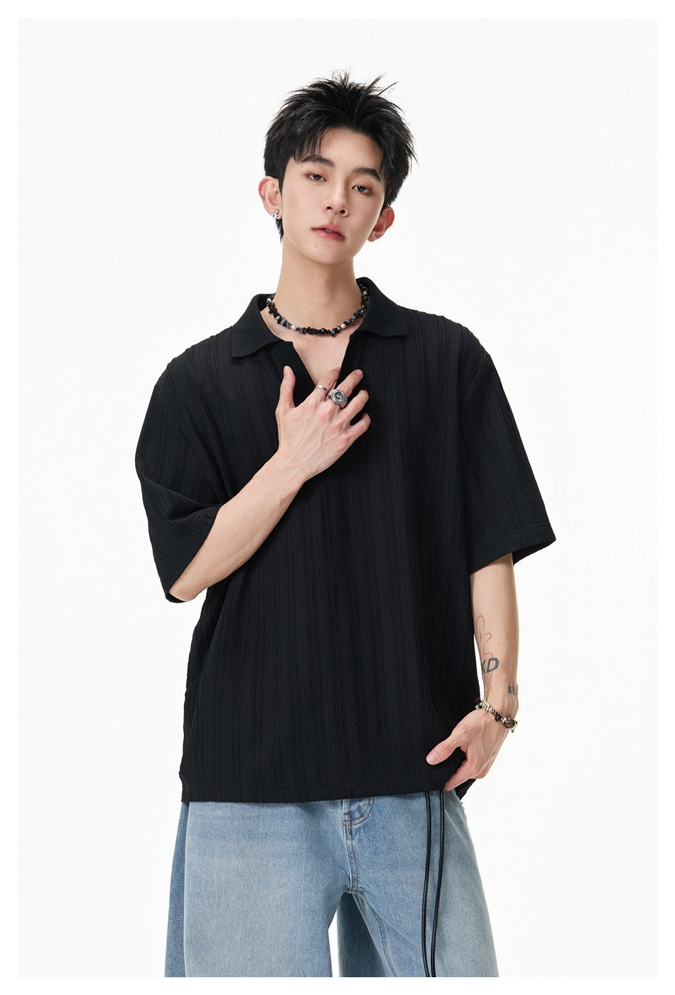 Model wearing a black textured short-sleeve polo with light blue jeans, shown from the front.