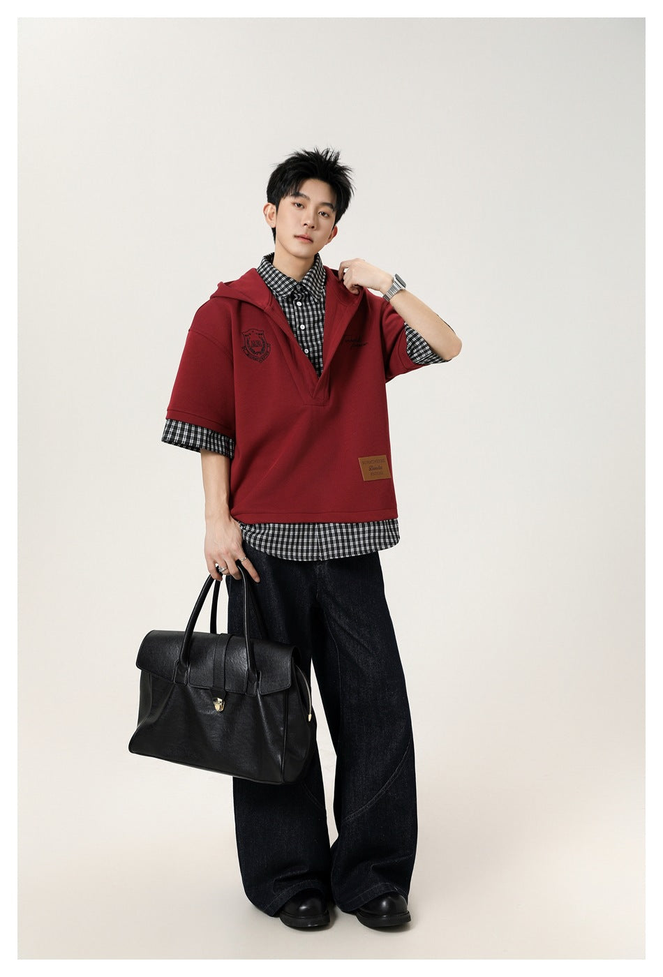 Model wearing a burgundy short-sleeve hooded top over a black-and-white checked shirt, with wide black trousers.