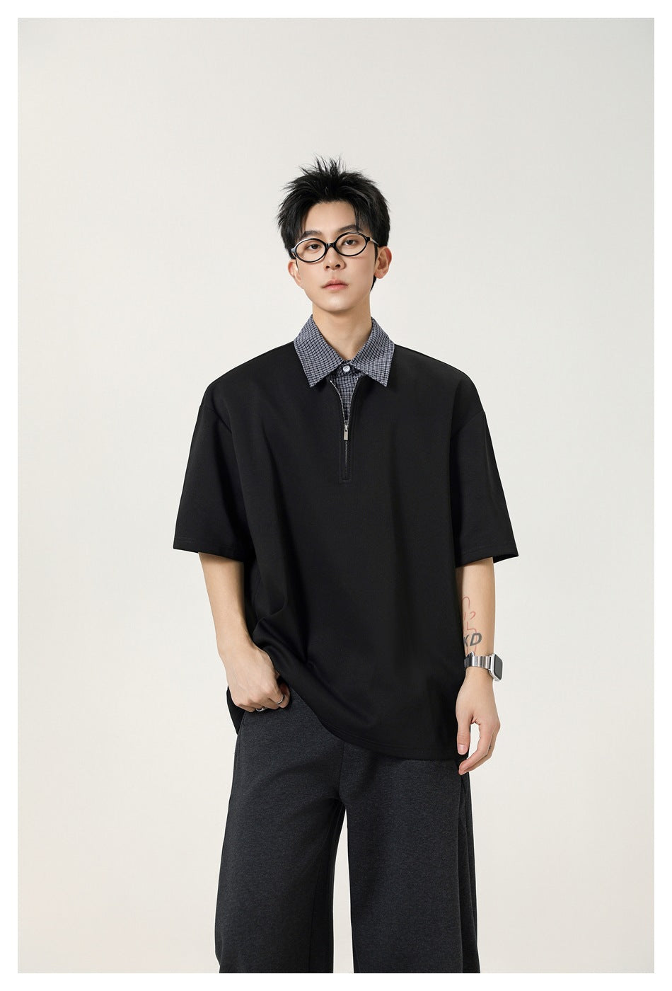 Male model wearing a black oversized short-sleeve top with a checked collar and short zip placket.