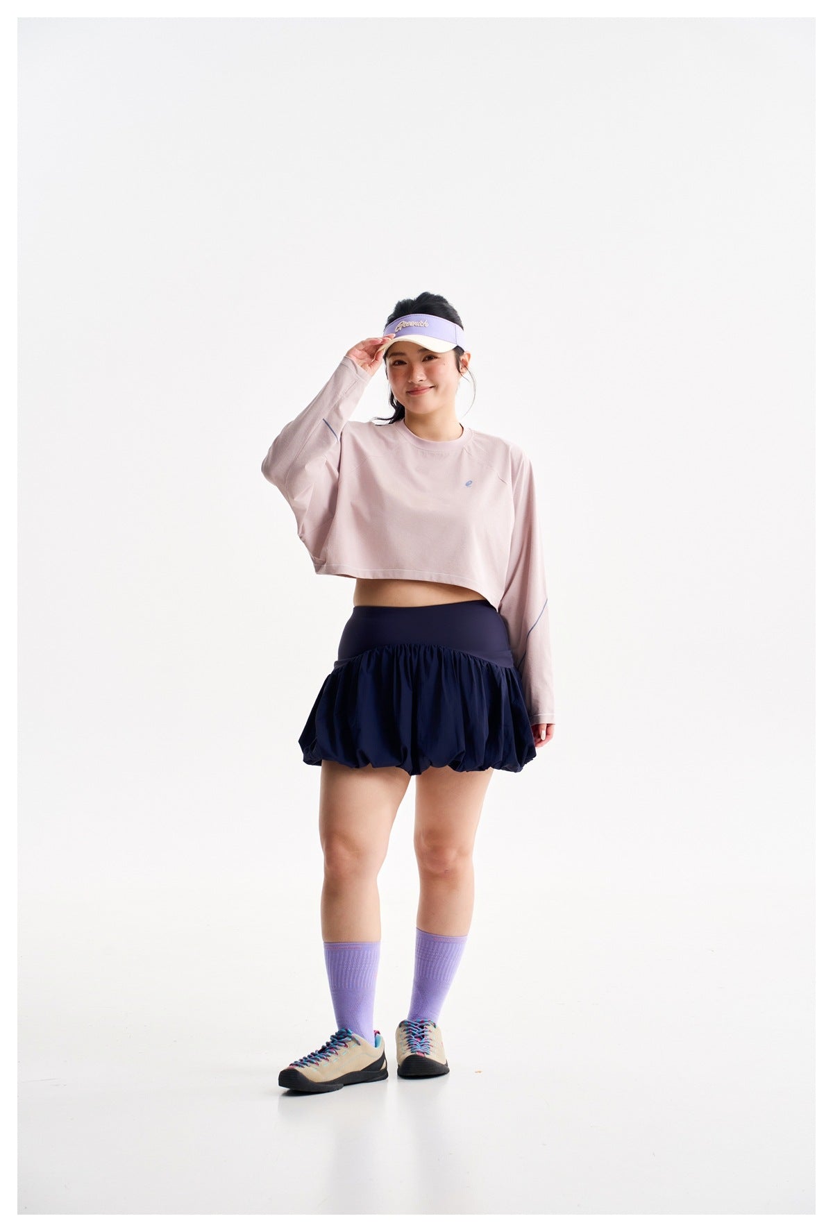 Model wearing a pale pink cropped long-sleeve top with a navy bubble-hem skirt in a studio.