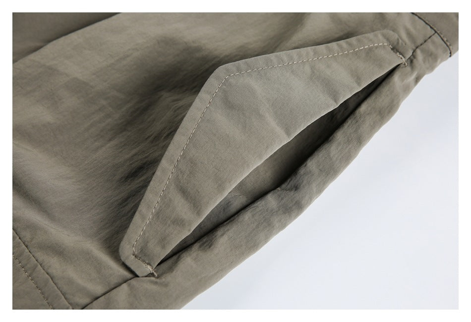 Close-up of a stitched flap pocket on olive-gray trousers.