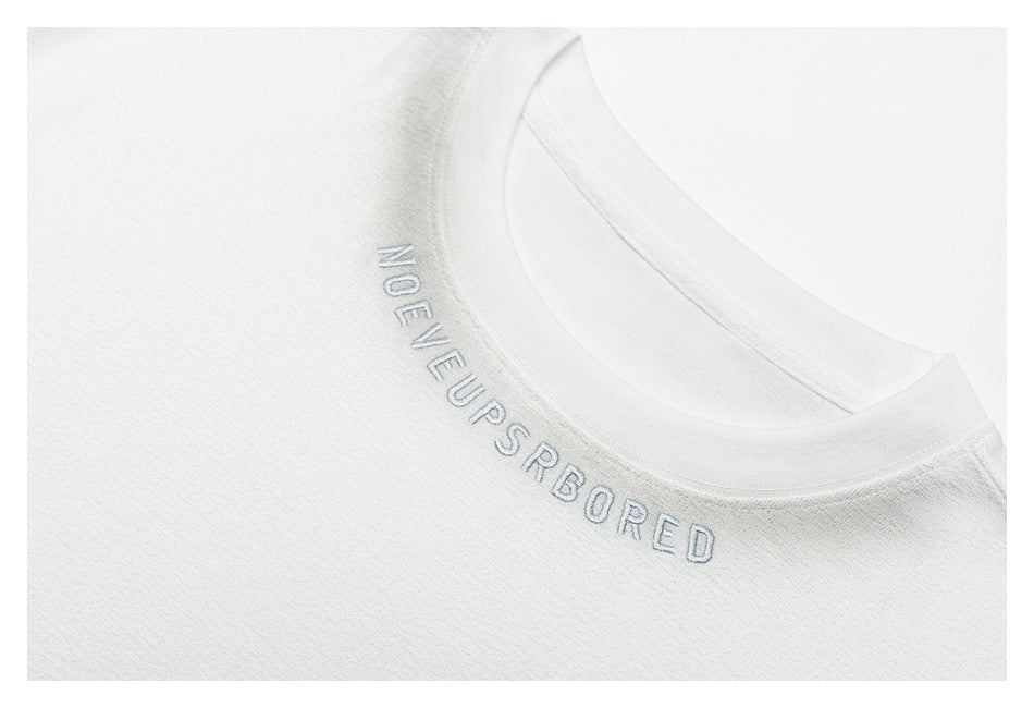 Close-up of a white crew neckline with small gray English lettering embroidered along the collar.