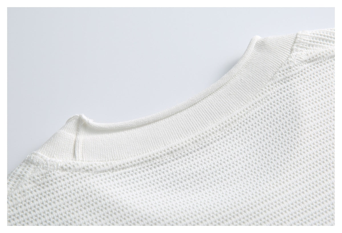 Close-up of a white knit garment's ribbed crew neckline and shoulder seam.