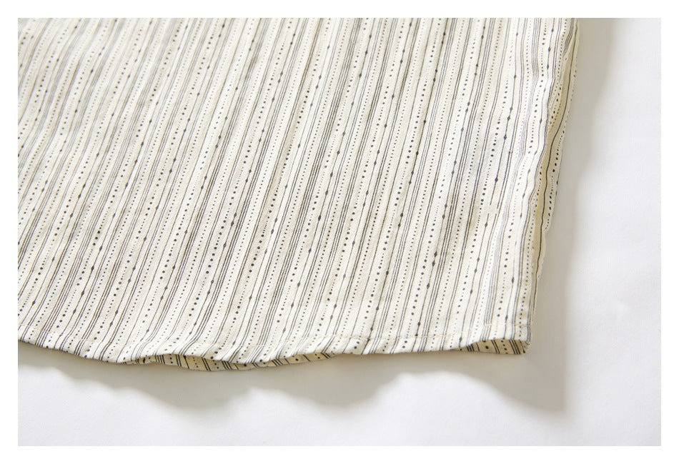 Close-up of a straight garment hem and side edge on ivory fabric with fine black dotted stripes.