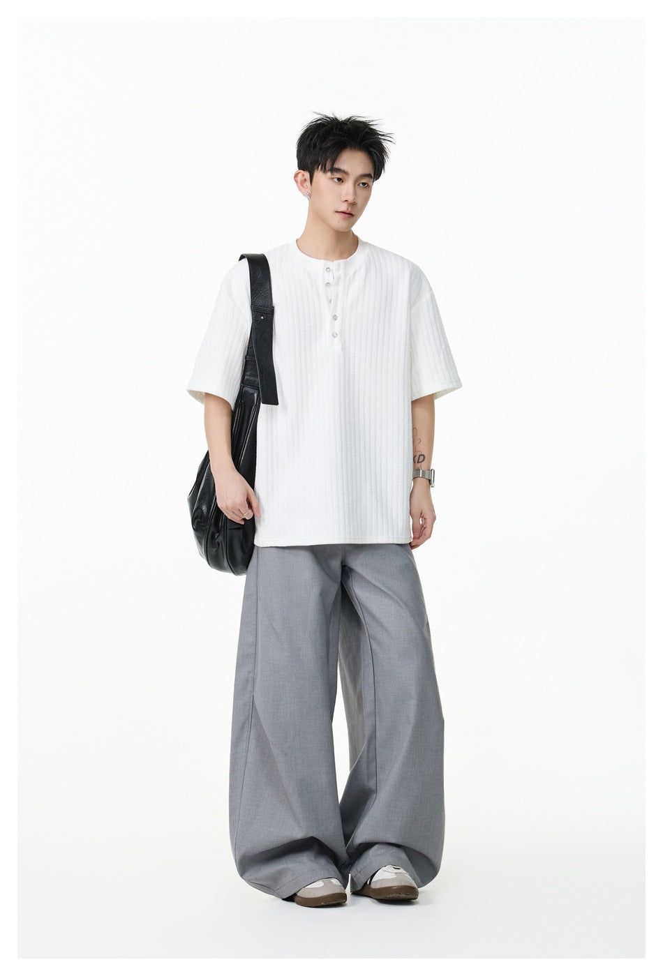 Model wearing a white short-sleeve ribbed Henley shirt with a button placket and gray wide-leg trousers, carrying a black