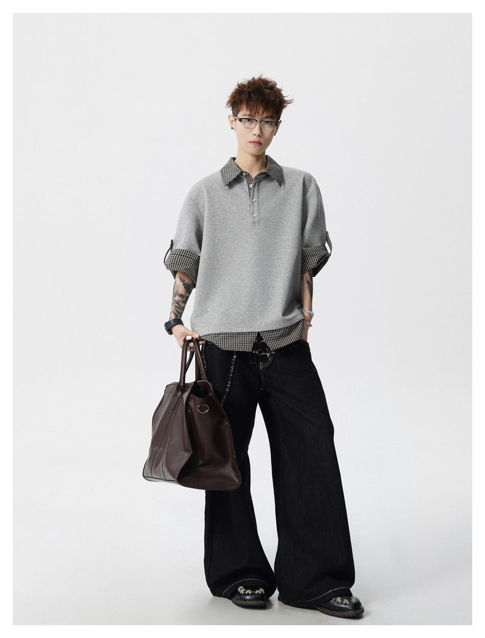 Full-length model wearing an oversized gray top with checked trim, wide black trousers, and carrying a brown bag.
