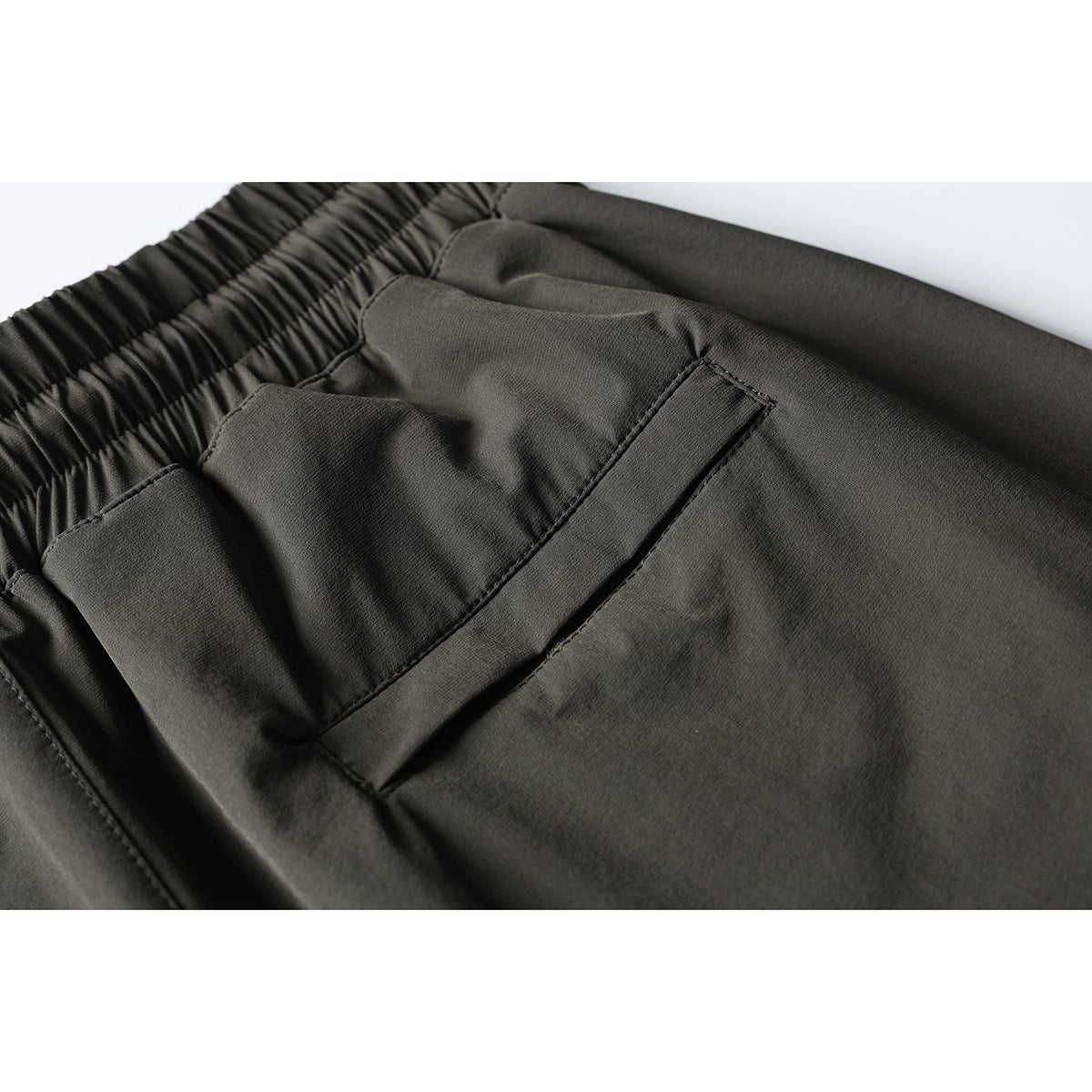 Close-up of dark olive pants showing an elastic waistband and a stitched rear pocket.