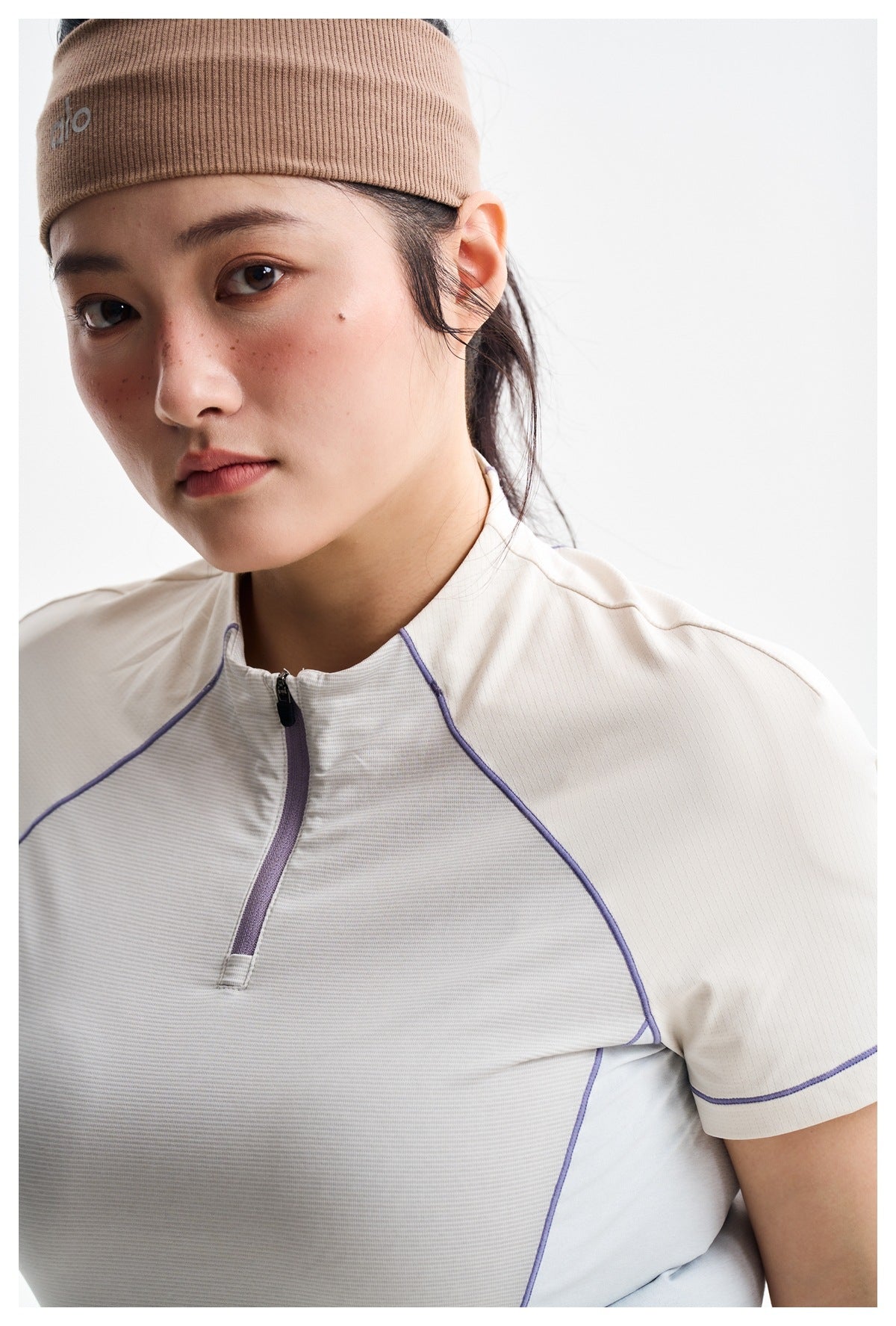 Close-up of a model wearing an ivory athletic shirt with lavender piping and a taupe ribbed headband.