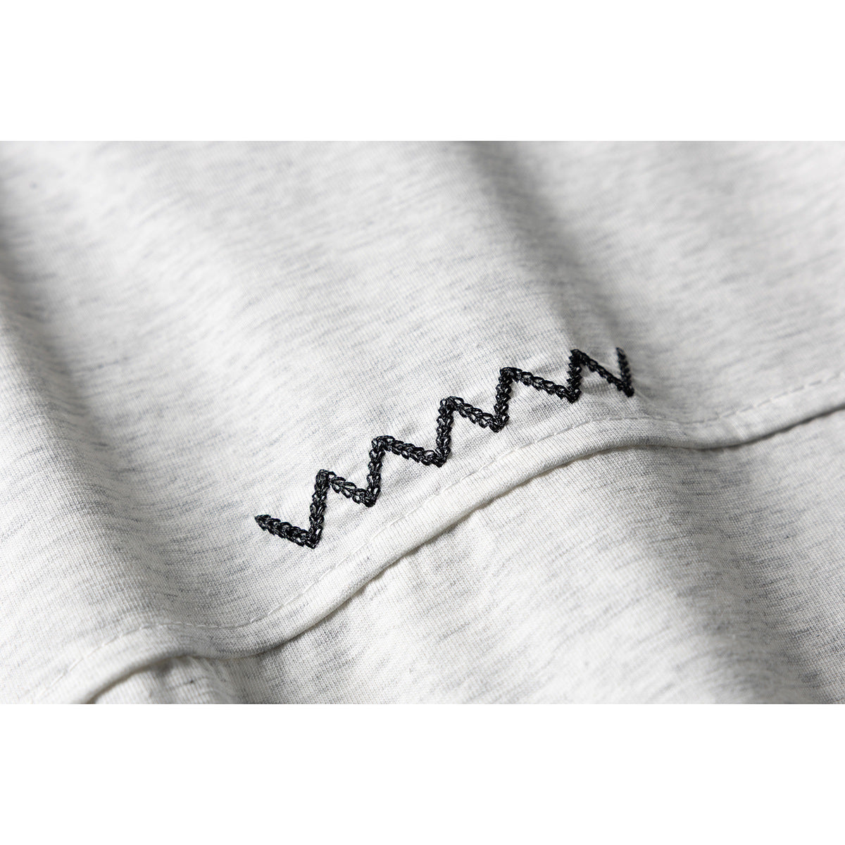 Close-up of black zigzag embroidery along a seam on light gray melange T-shirt fabric.