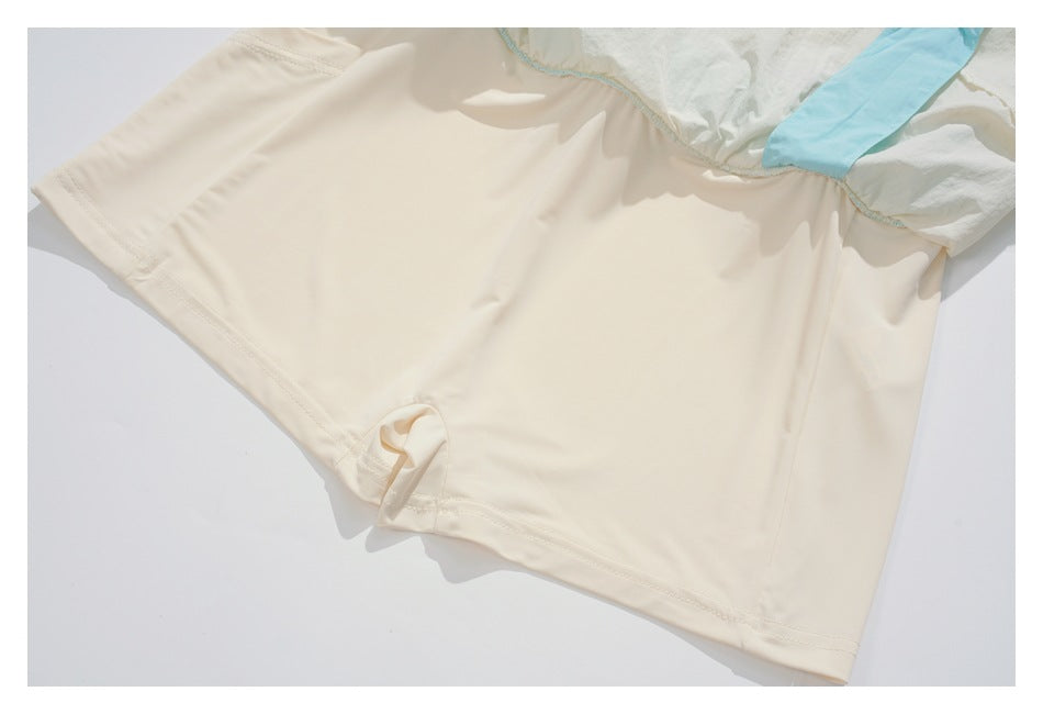 Close-up of an off-white garment hem and stitching, with a small fabric loop and light blue panel.