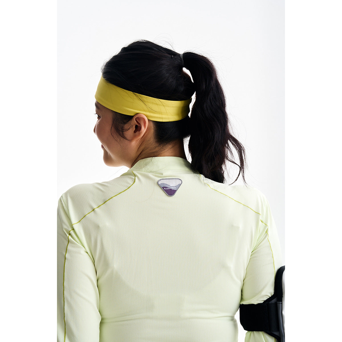Back view of a model in a pale yellow-green long-sleeve top with contrast seams and a yellow headband.