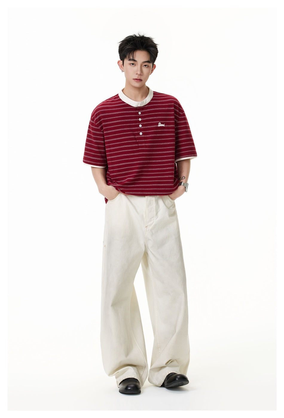 Model wearing a burgundy striped henley with cream trim and loose cream trousers, hands in pockets.