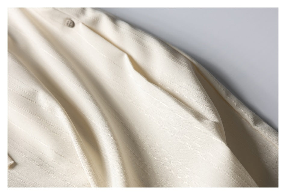 Close-up of cream striped trouser fabric with a small button and draped folds.