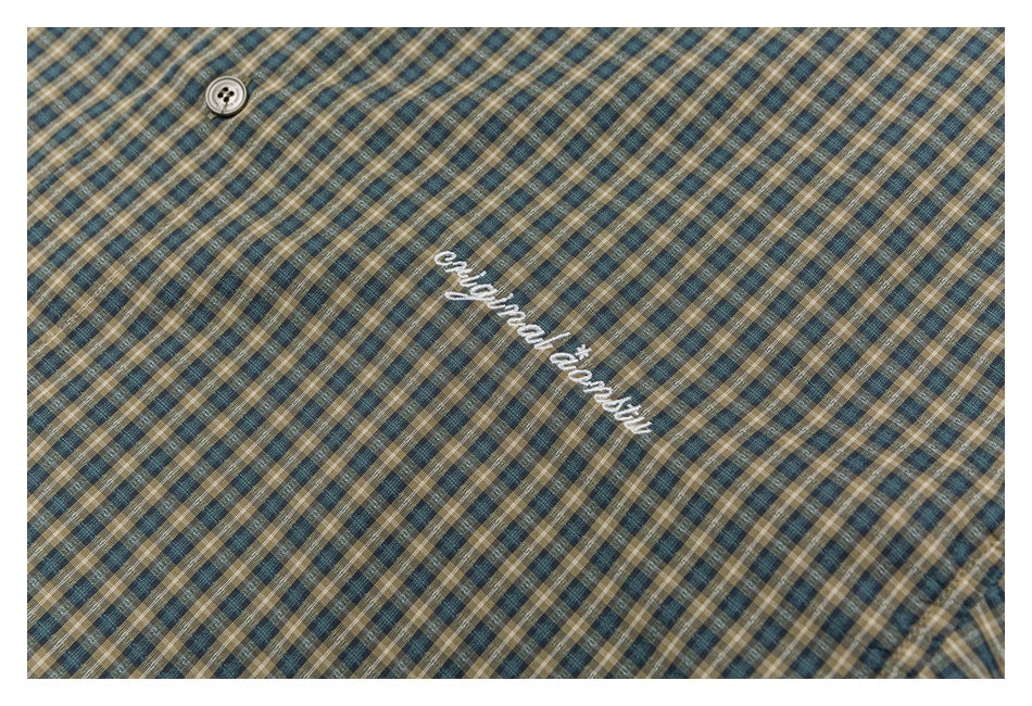Close-up of blue, tan, and cream plaid shirt fabric, a button, and white embroidered lettering.
