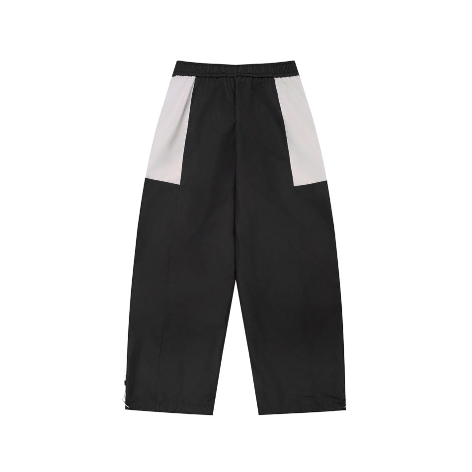 Front view of black wide-leg pants with white side panels, an elastic waistband and gathered ankle hems.