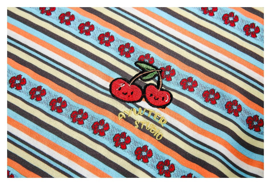 Close-up of embroidered smiling cherries and yellow lettering on striped knit fabric with red flower bands.