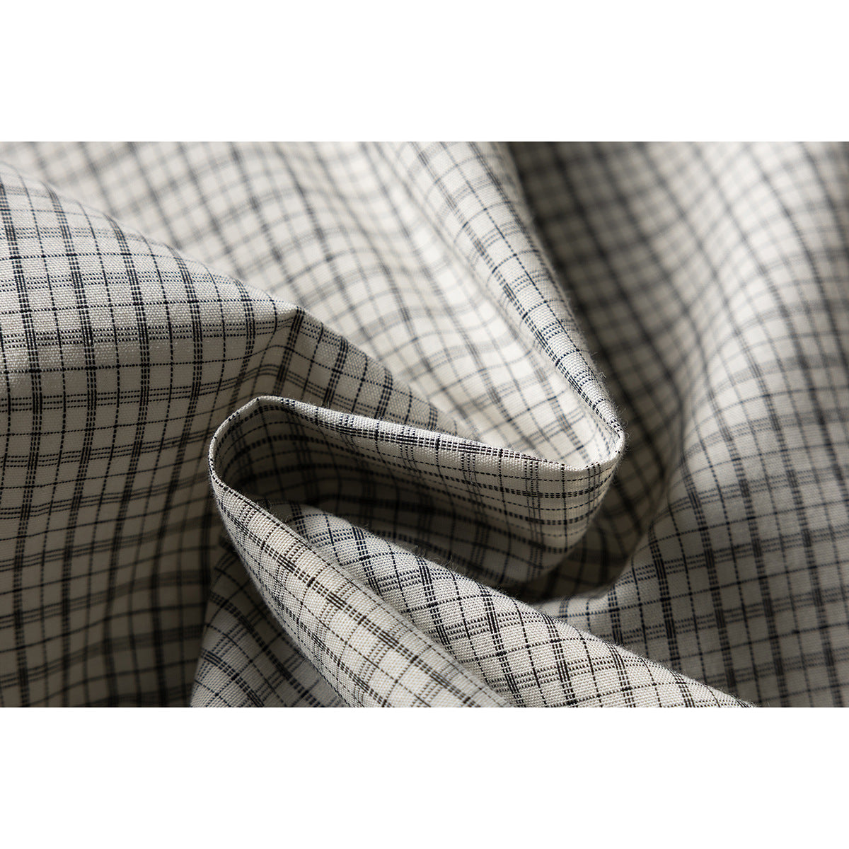Macro view of the cream shirt's fine black-and-gray plaid fabric folded into soft pleats.
