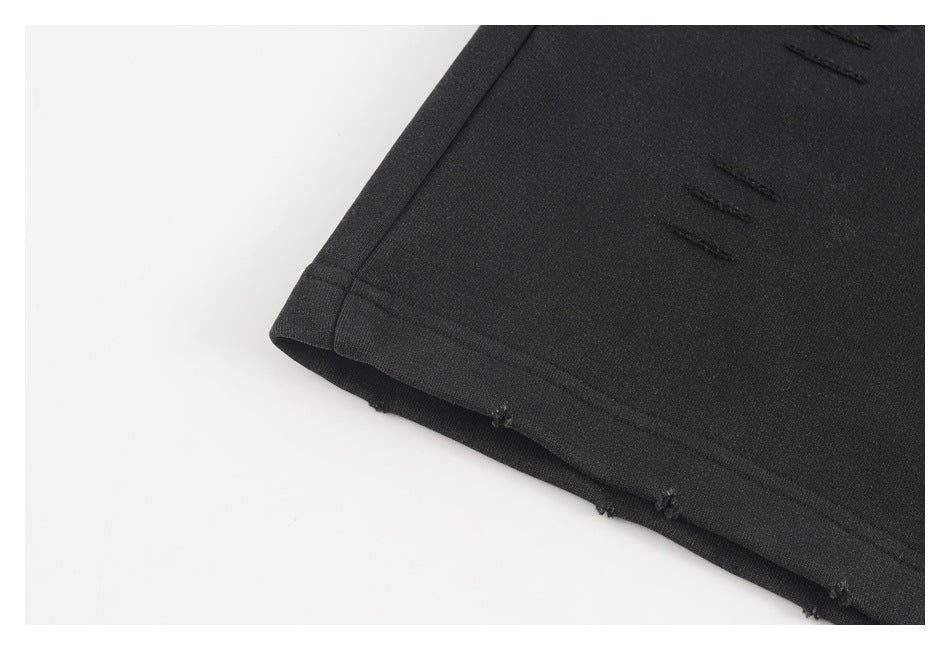 Close-up of a black pant leg hem with small distressed openings and double stitching.