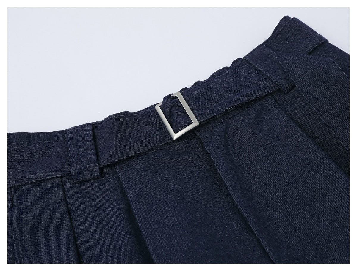 Close-up of the dark navy trouser waistband, belt loops, pleats, and rectangular silver buckle.