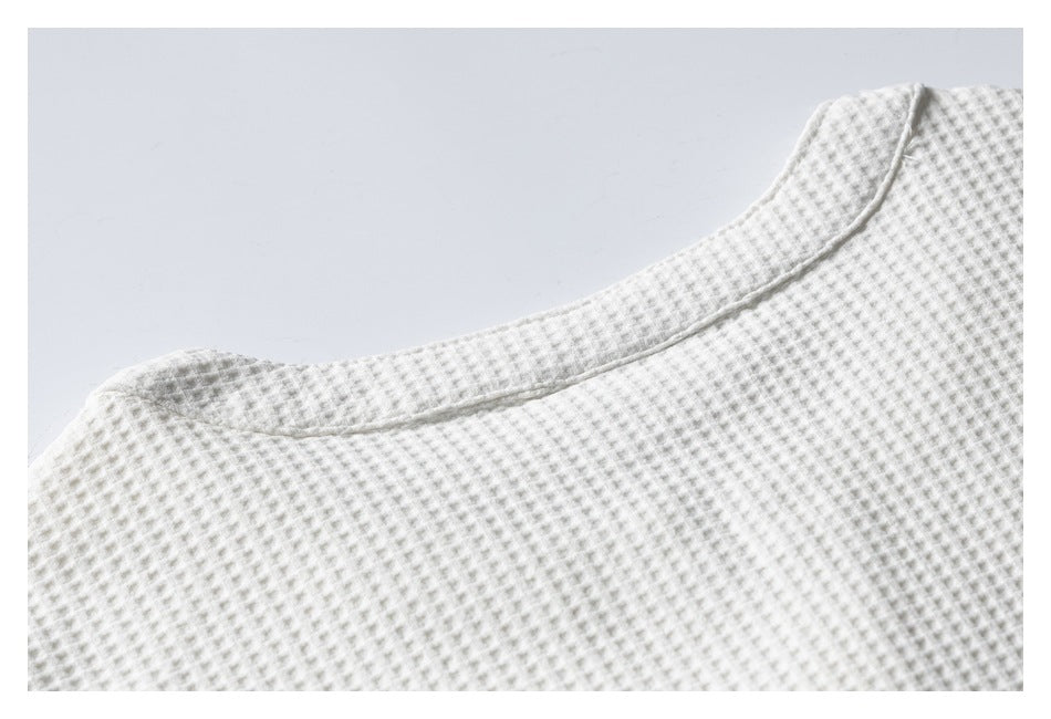 Close-up of the rounded neckline and stitching on an ivory waffle-knit garment.