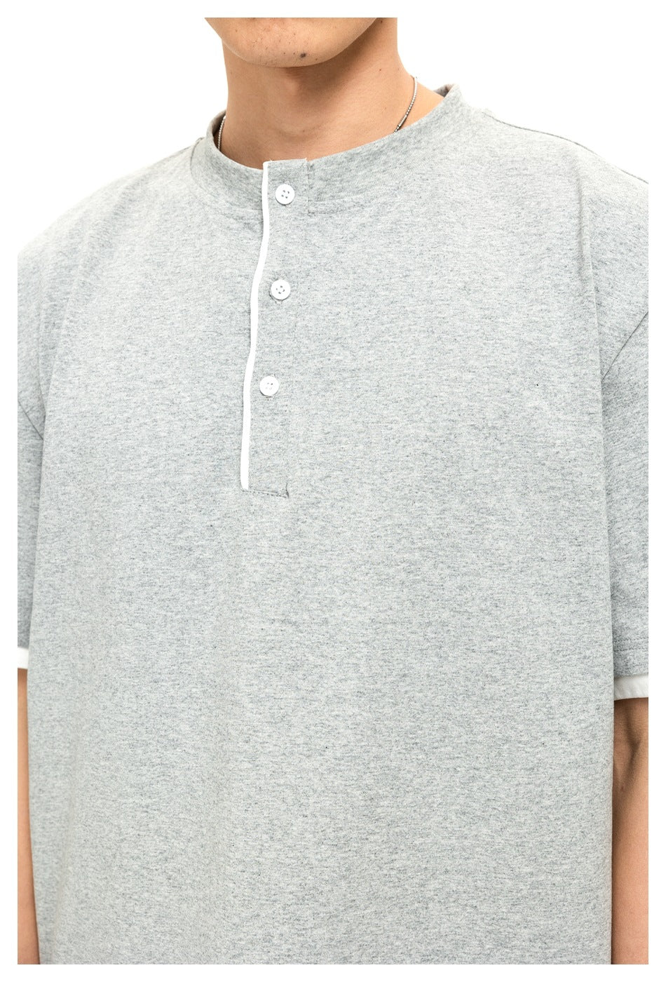 Close-up of a person wearing a light gray short-sleeve shirt with a band collar and three-button placket.
