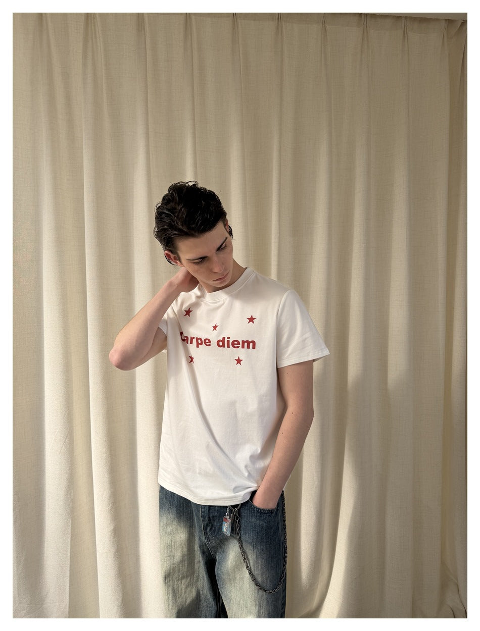 Model wearing a white crew-neck T-shirt with red “Carpe diem” text and stars, paired with faded jeans.