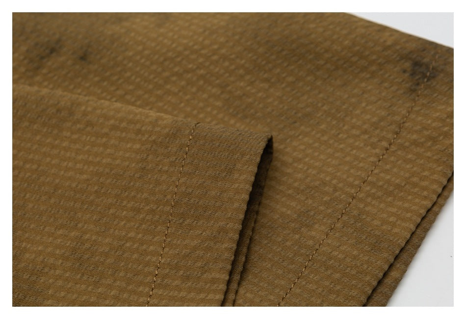 Close-up of the brown shirt's sleeve cuff and stitched edge against its subtly checked fabric.