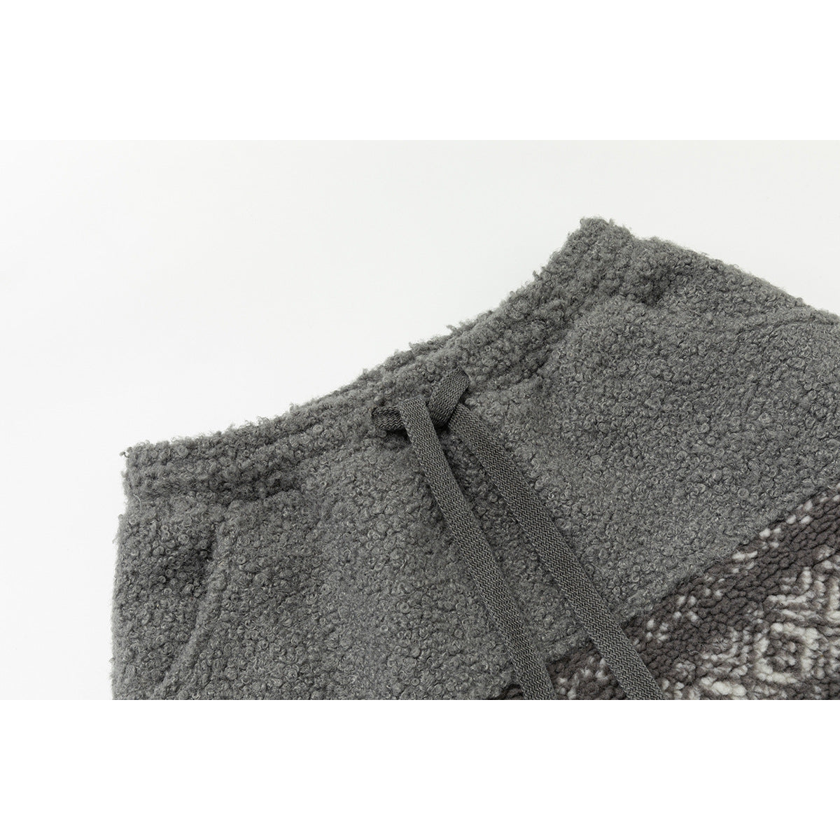 Close-up of a gray loop-textured garment waistband with dark drawstrings and a patterned panel at the edge.