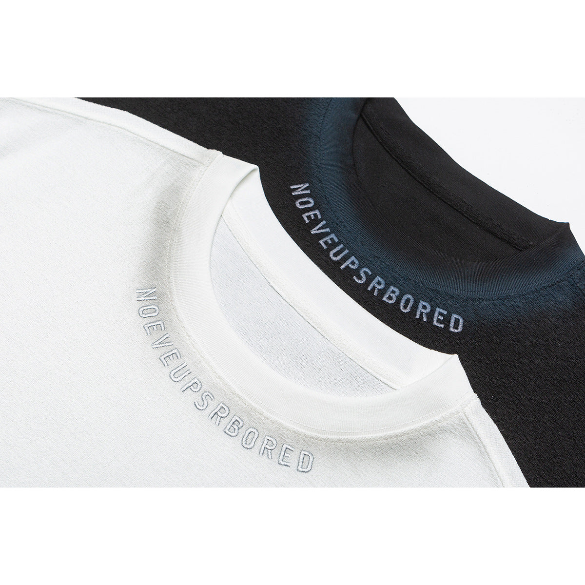 Close-up of white and black T-shirt crew necks with embroidered lettering.